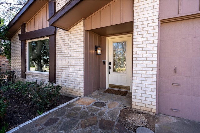 doorway to property featuring board and batten siding and brick siding