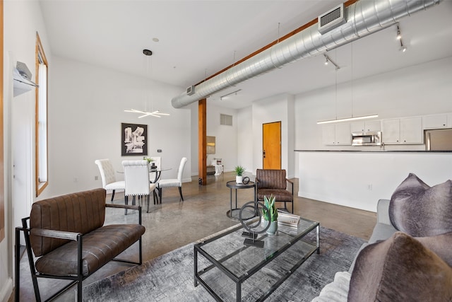 living area with concrete floors, a high ceiling, visible vents, and track lighting