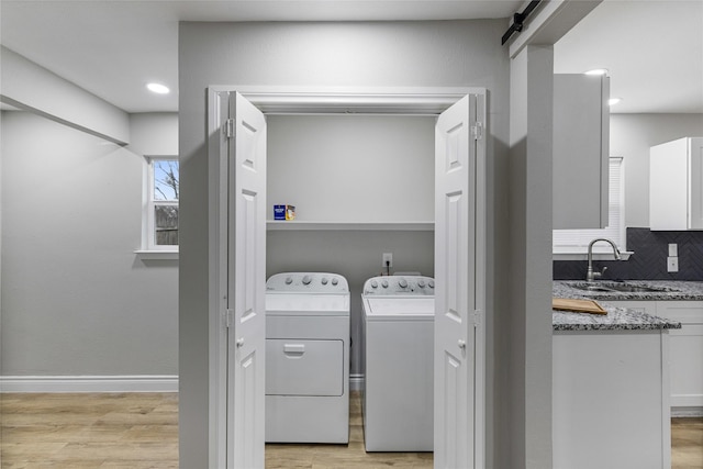 clothes washing area with a barn door, laundry area, a sink, light wood-type flooring, and washing machine and clothes dryer