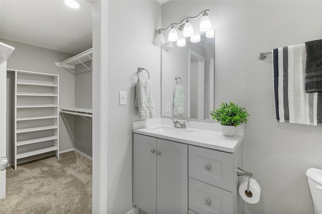 bathroom with toilet, a spacious closet, and vanity