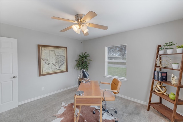 carpeted office space featuring a ceiling fan and baseboards