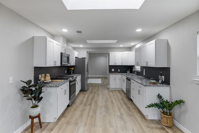 kitchen featuring a skylight, stainless steel appliances, visible vents, a sink, and dark stone countertops