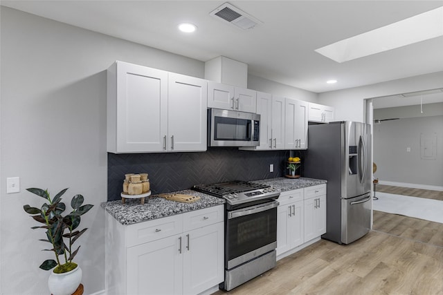 kitchen with stainless steel appliances, visible vents, decorative backsplash, stone countertops, and light wood-style floors