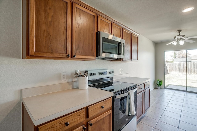 kitchen featuring brown cabinets, light tile patterned floors, light countertops, appliances with stainless steel finishes, and a ceiling fan