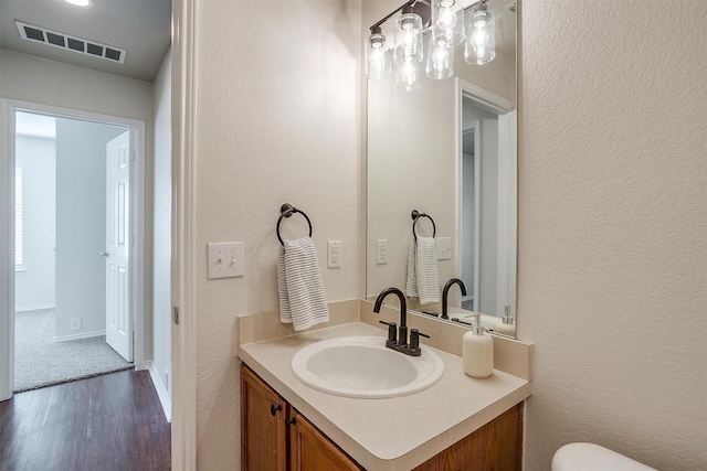 half bath featuring a textured wall, toilet, wood finished floors, vanity, and visible vents