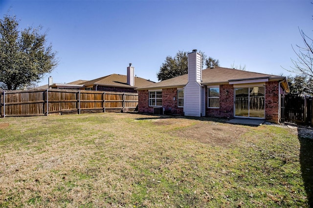 rear view of property with fence private yard, a chimney, a lawn, and brick siding