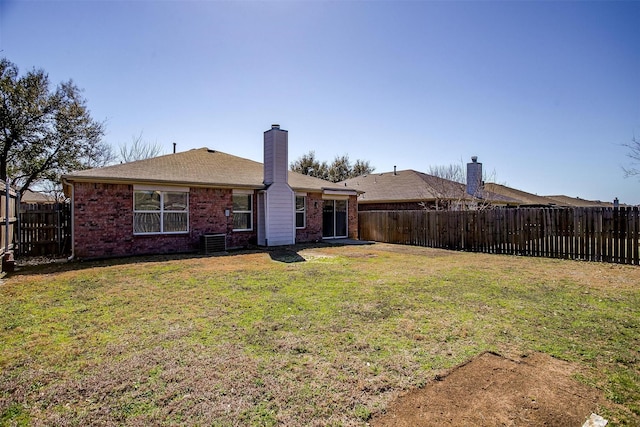 back of property featuring brick siding, a chimney, a lawn, cooling unit, and a fenced backyard