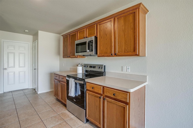 kitchen featuring appliances with stainless steel finishes, light countertops, brown cabinets, and light tile patterned floors