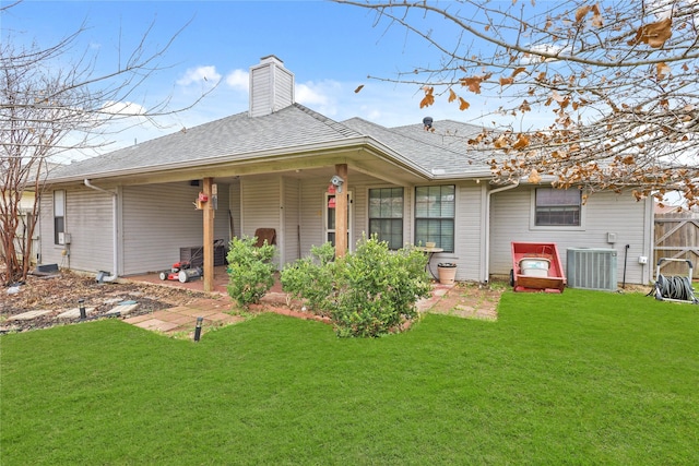 rear view of property featuring a yard, a chimney, a shingled roof, central AC unit, and fence