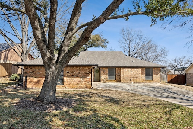 ranch-style house featuring brick siding, roof with shingles, concrete driveway, fence, and a front lawn