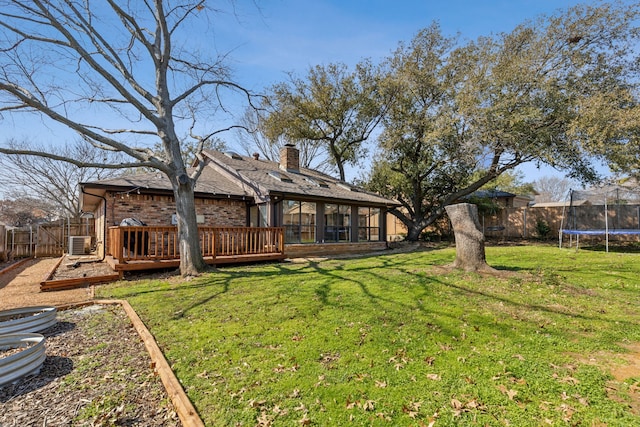 rear view of house featuring a trampoline, a fenced backyard, brick siding, and a chimney