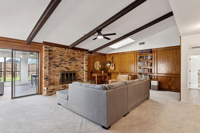 living room with a brick fireplace, wooden walls, lofted ceiling with skylight, and light colored carpet