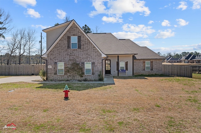 traditional home featuring brick siding, a front yard, fence, and a shingled roof