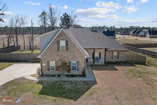 view of front of property featuring a shingled roof, a front yard, fence, and brick siding