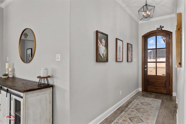 foyer with ornamental molding, a notable chandelier, baseboards, and wood finished floors