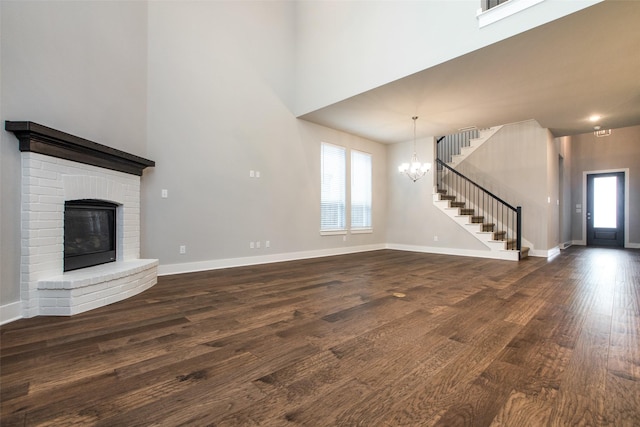 unfurnished living room featuring baseboards, dark wood-type flooring, stairs, a fireplace, and a notable chandelier