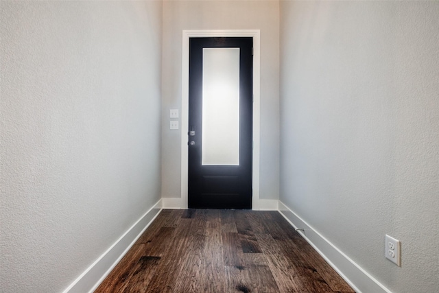 doorway to outside featuring dark wood-style floors, a textured wall, and baseboards