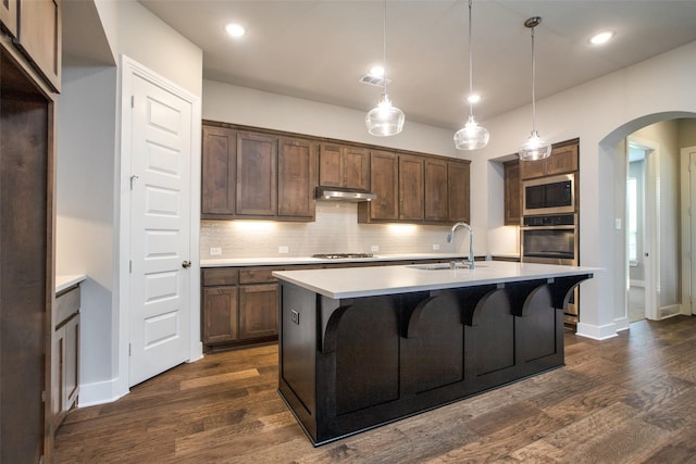 kitchen featuring arched walkways, under cabinet range hood, stainless steel appliances, a sink, and visible vents