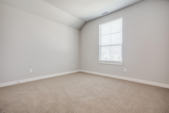 empty room featuring light carpet, vaulted ceiling, visible vents, and baseboards