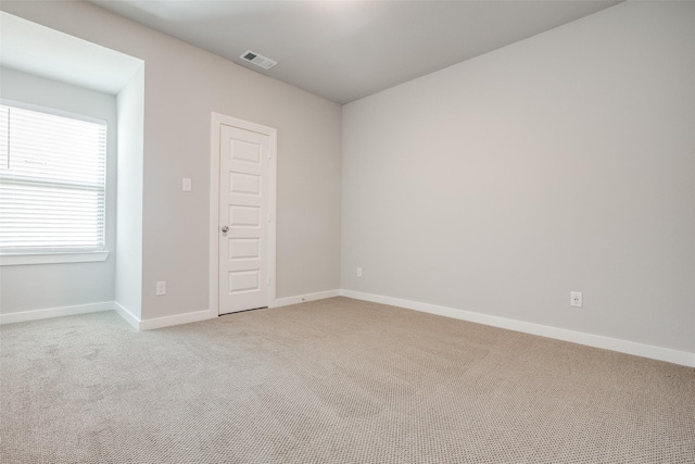 spare room with light colored carpet, visible vents, and baseboards