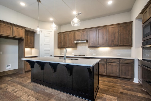 kitchen featuring stainless steel gas cooktop, a sink, under cabinet range hood, and dark wood-style flooring