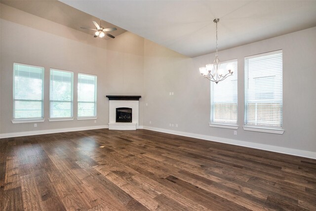 unfurnished living room with high vaulted ceiling, ceiling fan with notable chandelier, dark wood-type flooring, baseboards, and a brick fireplace