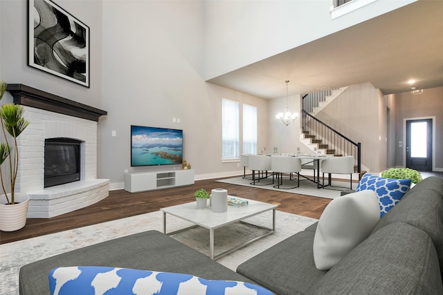 living room featuring a fireplace, wood finished floors, baseboards, stairway, and an inviting chandelier