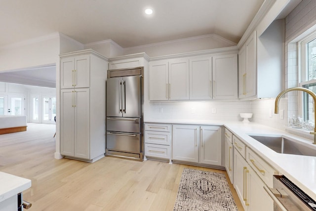 kitchen featuring stainless steel appliances, light countertops, light wood-style flooring, ornamental molding, and a sink