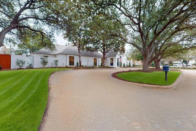 view of front of home featuring a front yard, curved driveway, and fence