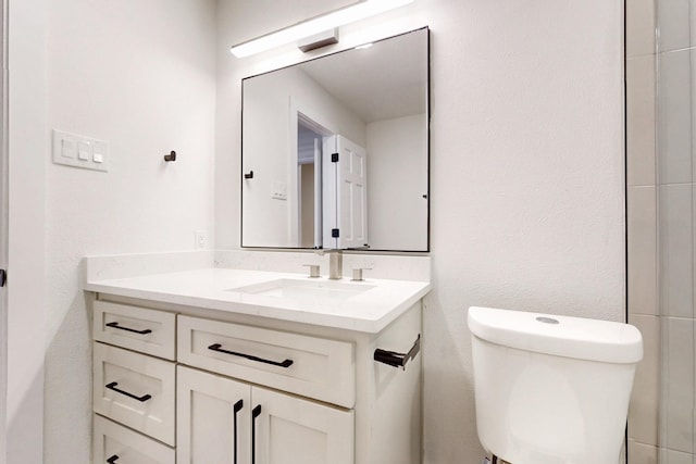 bathroom featuring toilet, a textured wall, and vanity