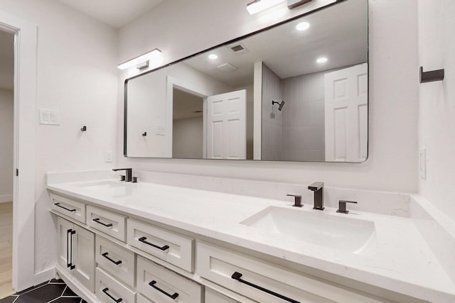 full bath featuring a tile shower, double vanity, a sink, and recessed lighting