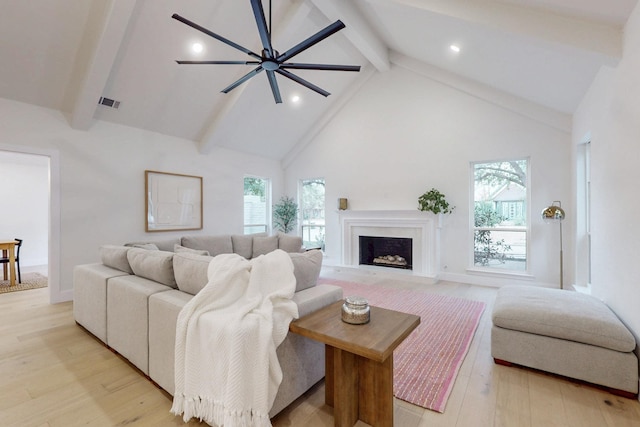 living room with light wood finished floors, visible vents, a fireplace with flush hearth, high vaulted ceiling, and beamed ceiling