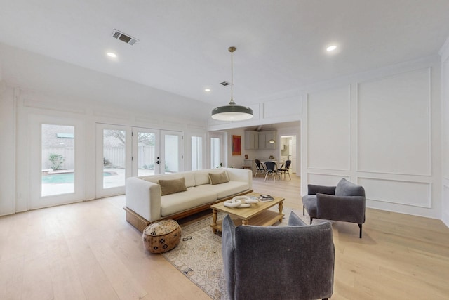 living area featuring french doors, visible vents, a decorative wall, and light wood finished floors