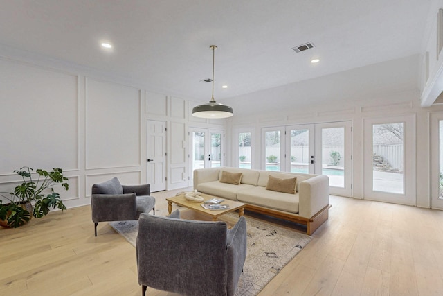 living area featuring light wood-type flooring, plenty of natural light, a decorative wall, and french doors