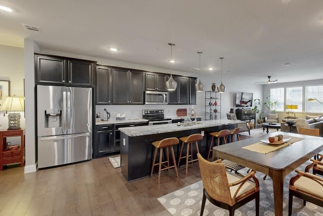 kitchen with stainless steel appliances, wood finished floors, an island with sink, and a sink