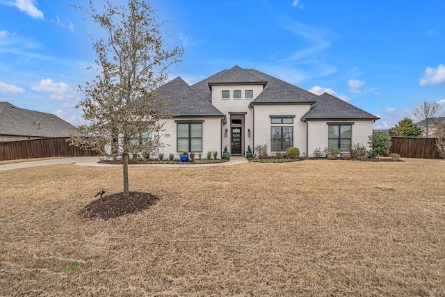 view of front of house with a shingled roof, a front yard, fence, and brick siding