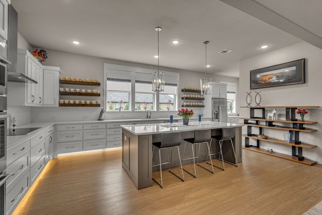 kitchen with open shelves, a kitchen island, a kitchen breakfast bar, light wood-type flooring, and pendant lighting