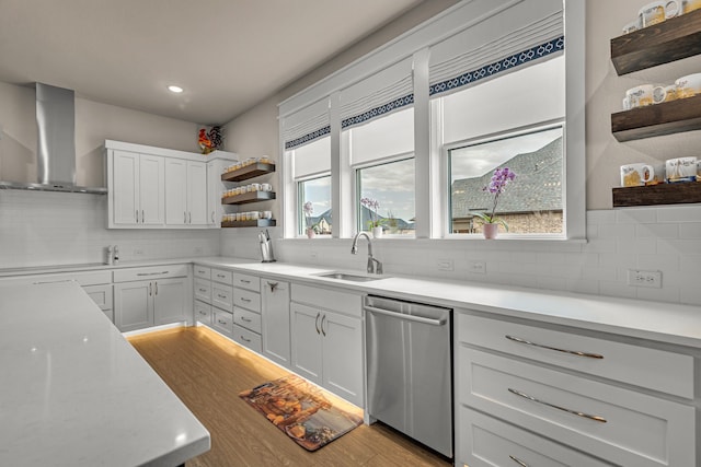 kitchen featuring light wood finished floors, wall chimney exhaust hood, stainless steel dishwasher, open shelves, and a sink