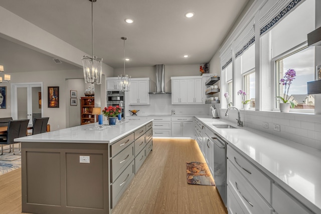 kitchen with a center island, light countertops, light wood-style floors, a sink, and wall chimney exhaust hood