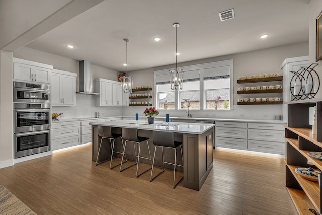 kitchen featuring a breakfast bar, open shelves, light countertops, visible vents, and wall chimney range hood