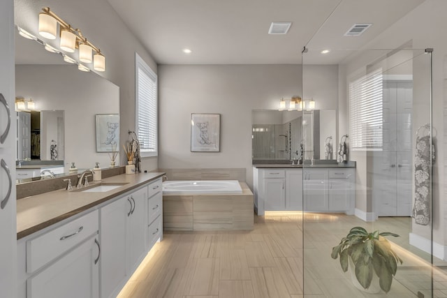 bathroom with two vanities, visible vents, a sink, a shower stall, and a bath