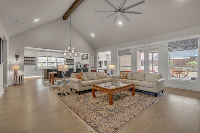 living room featuring ceiling fan with notable chandelier, high vaulted ceiling, beamed ceiling, and light wood-style flooring