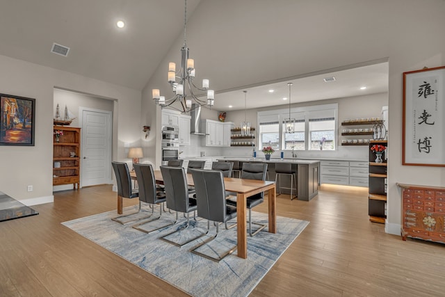 dining space with high vaulted ceiling, light wood finished floors, visible vents, and an inviting chandelier