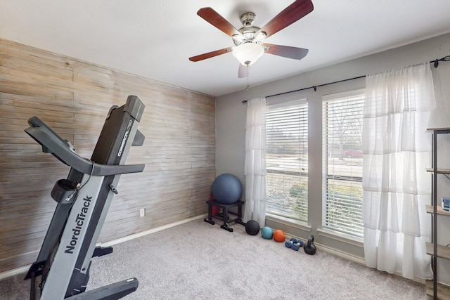 workout room with baseboards, carpet floors, wooden walls, and ceiling fan