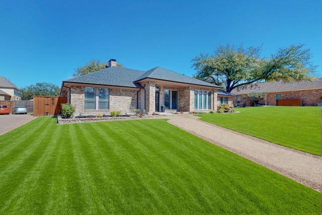 view of front of home featuring fence, a shingled roof, a chimney, a front lawn, and brick siding