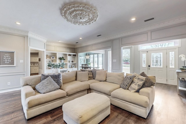 living room with a decorative wall, dark wood-type flooring, visible vents, and ornamental molding