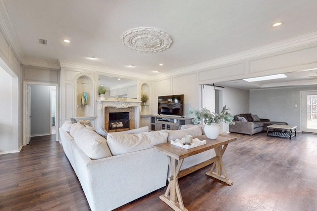 living area with visible vents, dark wood-style floors, a barn door, a fireplace, and crown molding