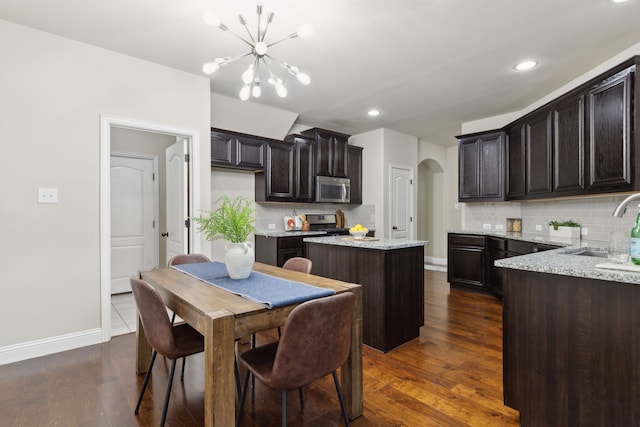 kitchen featuring arched walkways, a center island, stainless steel appliances, a sink, and dark brown cabinets