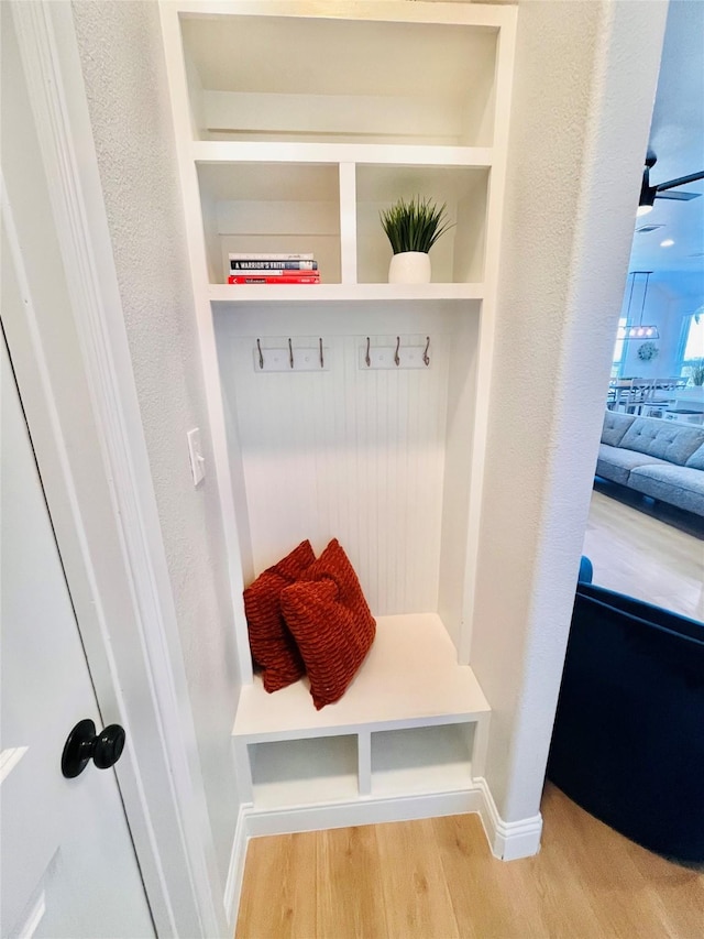 mudroom with baseboards, built in features, wood finished floors, and a textured wall