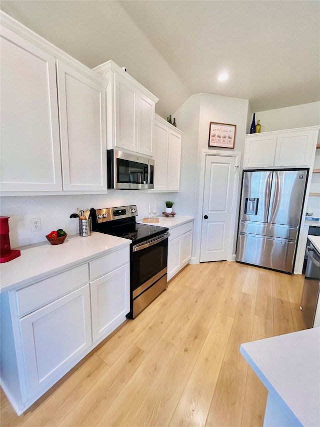 kitchen featuring white cabinets, lofted ceiling, appliances with stainless steel finishes, light countertops, and light wood-style floors